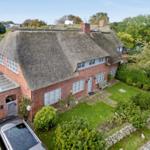 Red brick house with thatched roof, garden, and garage.
