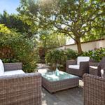 Terrace with wicker furniture and glass table under trees.