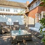 Terrace with wicker furniture and glass table in front of a thatched house.