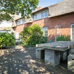 Backyard with stone bench, terrace, and red brick house with thatched roof.