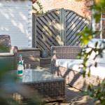 Terrace with wicker furniture, glass table, and bottle in sunlight.