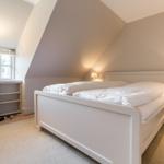 Bedroom with sloped ceiling, white bed, and window with view outside.