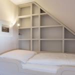 Bedroom with white bed and built-in shelf under sloped ceiling.