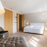 Bedroom with bed, wicker chair, and wooden floor.