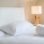 A bed with white linens and a bedside lamp with a wooden base.