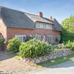 Red brick house with thatched roof and well-kept garden.
