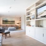Living room with sofa, chair, and TV area. Wooden floor and bookshelves.