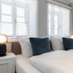 Schlafzimmer mit Doppelbett, zwei Nachttischen und Lampe. Fenster mit Jalousien.