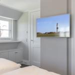 Schlafzimmer mit Bett, Fenster und Wandbild eines Leuchtturms.