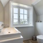 Badezimmer mit Waschbecken, Toilette und Fenster mit Blick auf Wald.