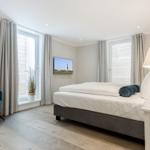 Schlafzimmer mit Bett, blauer Sessel und Fenstern.