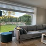 Großes Wohnzimmer mit grauem Sofa, blauem Hocker und Blick auf den Garten.