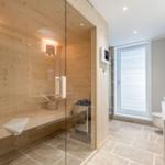 Dusche mit Glaswand, Holzsauna und Waschbecken im Badezimmer.