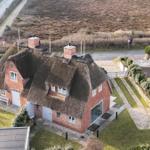 Rotes Haus mit Strohdach und Garten. Nebenhaus mit blauem Dach.