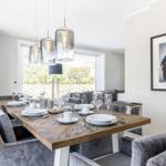 Esszimmer mit Holztisch, grauen Stühlen und Glaslampen. Wandbild und Fenster mit Gartenblick.