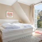 Schlafzimmer mit Dachschrägen, weißem Bett und Balkonzugang.