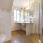 Badezimmer mit Dusche, Waschbecken und Toilette. Fenster sorgt für Tageslicht.