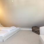 Schlafzimmer mit Dachschrägen, weißem Bett und Streifen-Sofa.