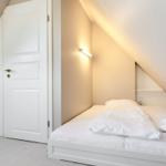 Schlafzimmer mit Dachschrägen, weißem Bett und Kleiderschrank.