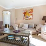 Wohnzimmer mit Sofa, Sessel und Glas-Tisch. Weiße Kaminwand und Wandbild.