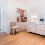 Bedroom with bed, chair, and wall art. Wooden floor and white walls.