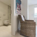 Hallway with chair and view into bathroom. Wall art and door with glass panel.
