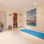 Fitness room with yoga mat, ball, and dumbbells. Sauna in background. Wall picture with pool motif.