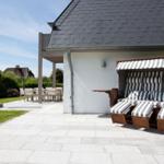 Terrace with beach lounger, table and chairs. Backyard with lawn and flowers.