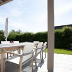 Terrace with table and chairs, surrounded by greenery and flowers.
