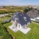 House with terrace and garden, surrounded by greenery and dunes.