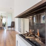 Fireplace with burning logs, adjacent living and dining area with wooden floor and furniture.