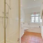 Badezimmer mit Dusche, Badewanne und Toilette. Terrakottafußboden und Fenster mit Vorhang.