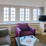 Wohnzimmer mit Fensterfront, Sitzgelegenheiten und Fernseher.
