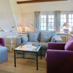 Wohnzimmer mit grauem Sofa, zwei violett gefärbten Sesseln und Glas-Tisch. Holzfußboden und große Fenster.