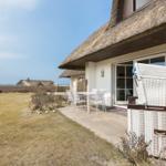 House with thatched roof, terrace with table and chairs, white wicker basket, view of beach and horizon.