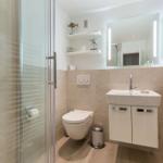 Bathroom with shower, sink, and toilet. Tiled wall and wooden floor.