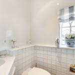 Badezimmer mit Waschbecken, Toilette und Fenster mit Blumen.