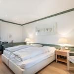 Schlafzimmer mit Doppelbett, Nachttisch und Stuhl. Fenster mit Vorhang. Wanddekoration.