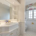 Badezimmer mit Waschbecken, Spiegel und Fenster mit Vorhang.