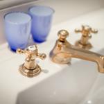 Waschbecken mit goldenen Wasserhähnen und zwei blauen Gläsern.