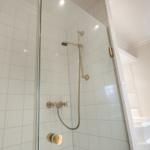 Dusche mit Glaswand, goldfarbenen Armaturen und weißen Fliesen.