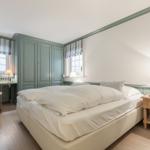 Schlafzimmer mit Bett, Nachttisch, Schrank und Fenstern mit Rollläden.