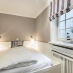 Schlafzimmer mit Bett, Nachttischlampen und Fenster mit Segelbootmodell.