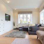 Wohnzimmer mit Sofa, Sessel, TV und Fenstern.