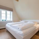 Schlafzimmer mit weißem Bett, Holzboden und Fenster mit Blick nach draußen.