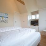 Schlafzimmer mit Doppelbett, Kleiderschrank und Fernseher an der Wand.