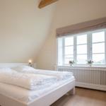 Schlafzimmer mit weißem Bett, Fenster und Holzboden.