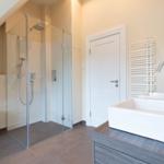 Moderne Dusche mit Glaswand, Waschtisch und Toilette in einem hellen Badezimmer.