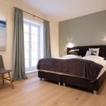 Schlafzimmer mit Bett, Fenster und Stuhl. Wandbild und Beleuchtung.