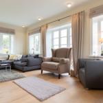 Wohnzimmer mit Sofa, Sessel und Fenstern. Holzboden und Teppiche.